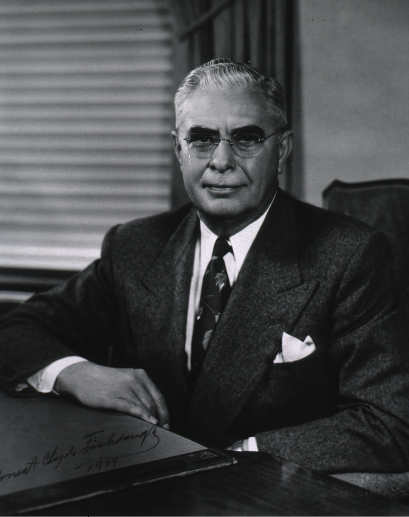 Portrait of Dr. Fishbaugh, another older white man wearing glasses and a suit